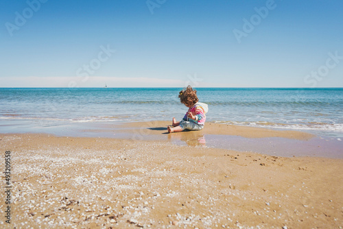 Wide view of a little girl wearing rainbow hoodie playing at the beach