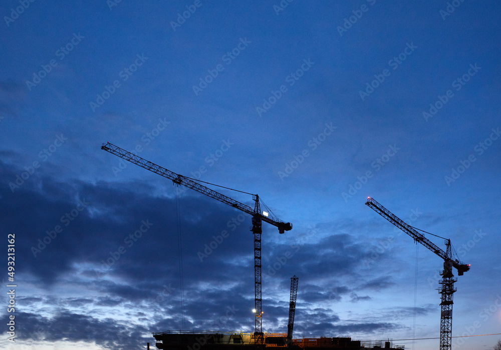 Budowa apartamentowca z dźwigiem budowlanym podczas budowy na tle błękitnego wieczornego nieba z chmurami Budowa apartamentowca z dźwigiem budowlanym podczas budowy na tle błękitnego wieczornego nieba z chmurami