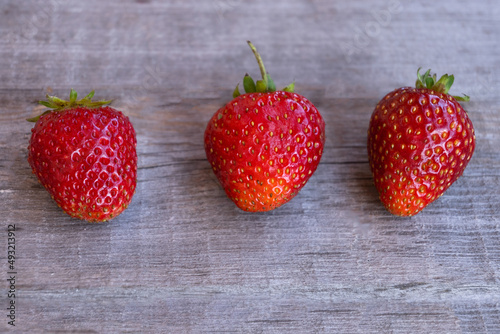 Three ripe strawberries lie on a wooden surface. Summer, strawberry season.
