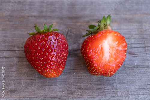 Two ripe strawberries lie on a wooden surface. A piece has been bitten off from one berry. Temptation.