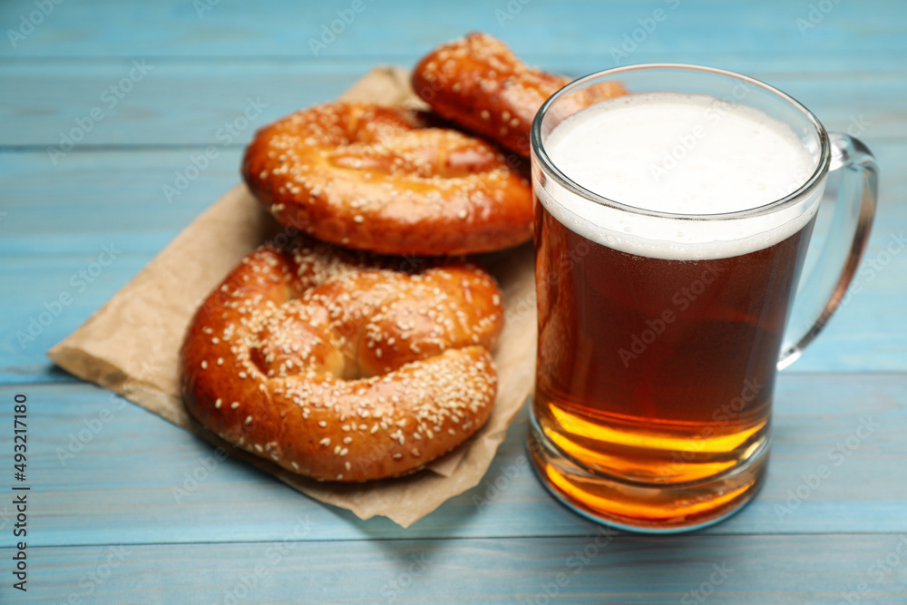 Mug of beer with tasty freshly baked pretzels on light blue wooden table, closeup Mug of beer with tasty freshly baked pretzels on light blue wooden table, closeup