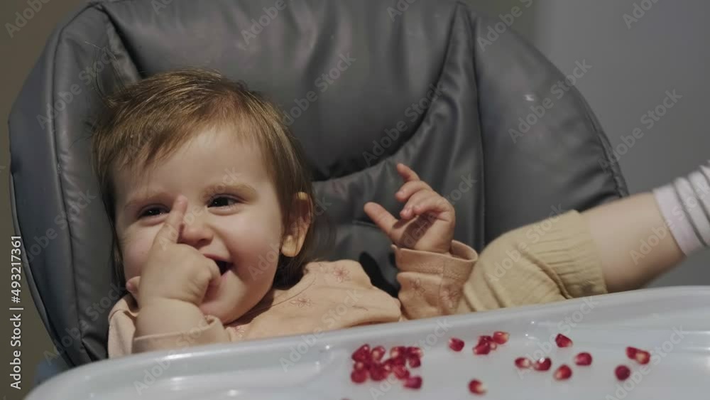 Portrait of happy young baby girl in high chair with pomegranate seeds on the table. Smiling happy child. Organic food. Sweet food. Portrait of happy young baby girl in high chair with pomegranate seeds on the table. Smiling happy child. Organic food. Sweet food.