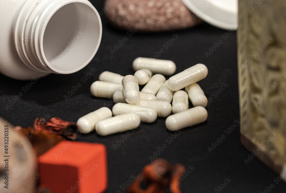 White bottle of supplements with white capsules on a black background White bottle of supplements with white capsules on a black background