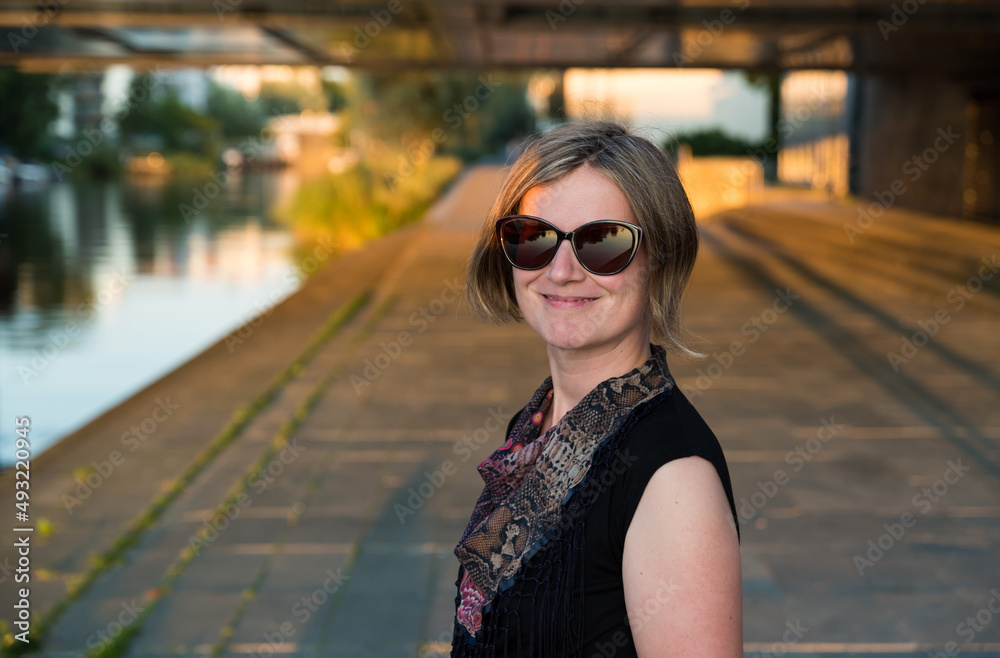 Portrait of a smiling thirty year old white woman under a bridge in Stockholm during sunset with warm light on her face