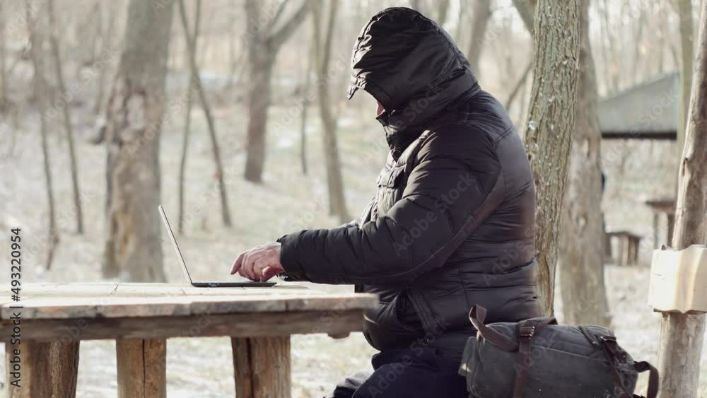 tourist typing on laptop at table in early spring forest, side view, remote work concept tourist typing on laptop at table in early spring forest, side view, remote work concept