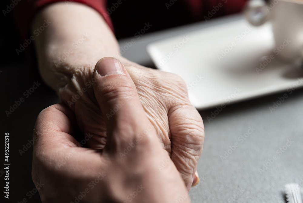 Close up of the hands of a 43 year old white man holding the hands of his 83 year old mother Close up of the hands of a 43 year old white man holding the hands of his 83 year old mother