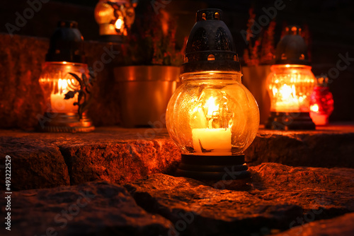 Fotografie, Obraz Different grave lanterns with burning candles on stone surface at night