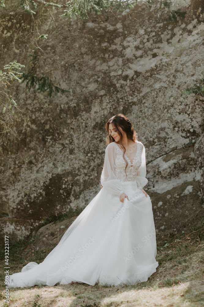 beautiful bride stands on rocks in a glamorous white wedding dress