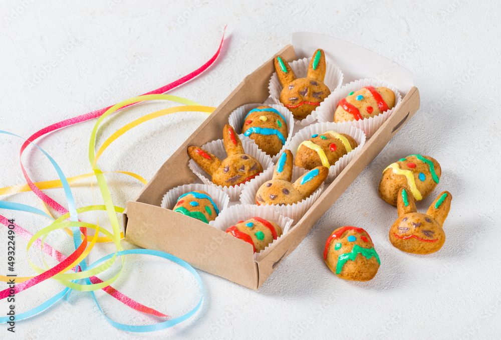 Easter cookies in the shape of eggs and rabbits, decorated with multicolored icing sugar, in a serving box. Light background