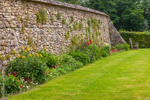 Parterre de fleurs d'été au pied d'un vieux mur en pierre devant une pelouse verte