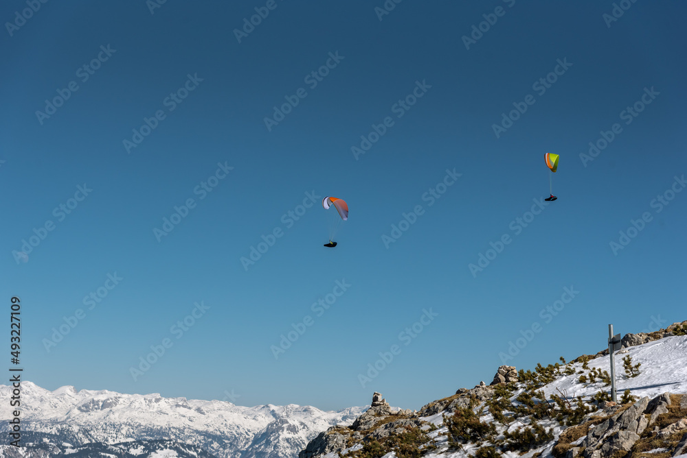 paraglider in front of snows alpine mountain range with clear blue sky