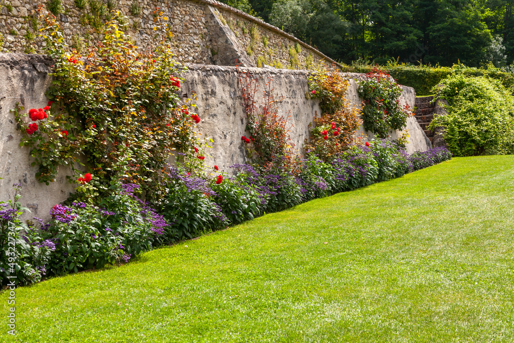 Parterre de fleurs d'été au pied d'un vieux mur en pierre devant une pelouse verte Parterre de fleurs d'été au pied d'un vieux mur en pierre devant une pelouse verte