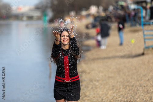 Mid-Motion shot: smiling teen girl sitting on the shore of lake and throwing water in the air