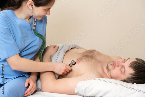 The doctor auscultizes the heart of a 30-year-old male patient with a phonendoscope, diagnosing heart disease in humans