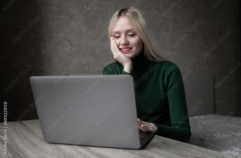 Happy smiling blonde girl in green golf joyfully works online at home with a laptop. Sits at the table in a good mood in the room. High quality photo Happy smiling blonde girl in green golf joyfully works online at home with a laptop. Sits at the table in a good mood in the room. High quality photo