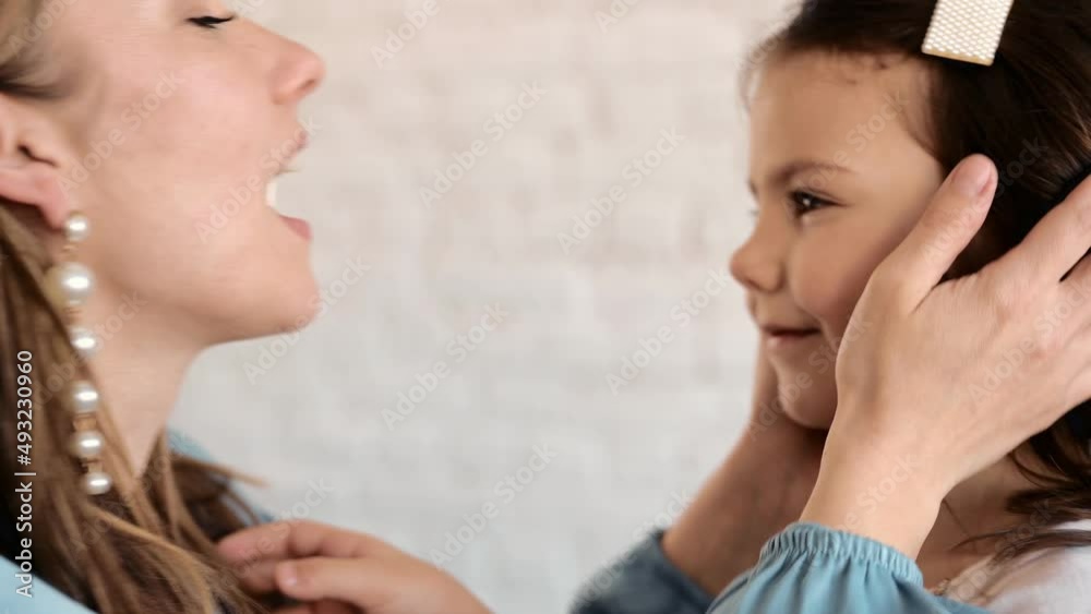 Loving tender young mum holding adorable cute girl daughter embracing kissing small kid. Happy affectionate mother cuddling with infant child standing at home. Light background
