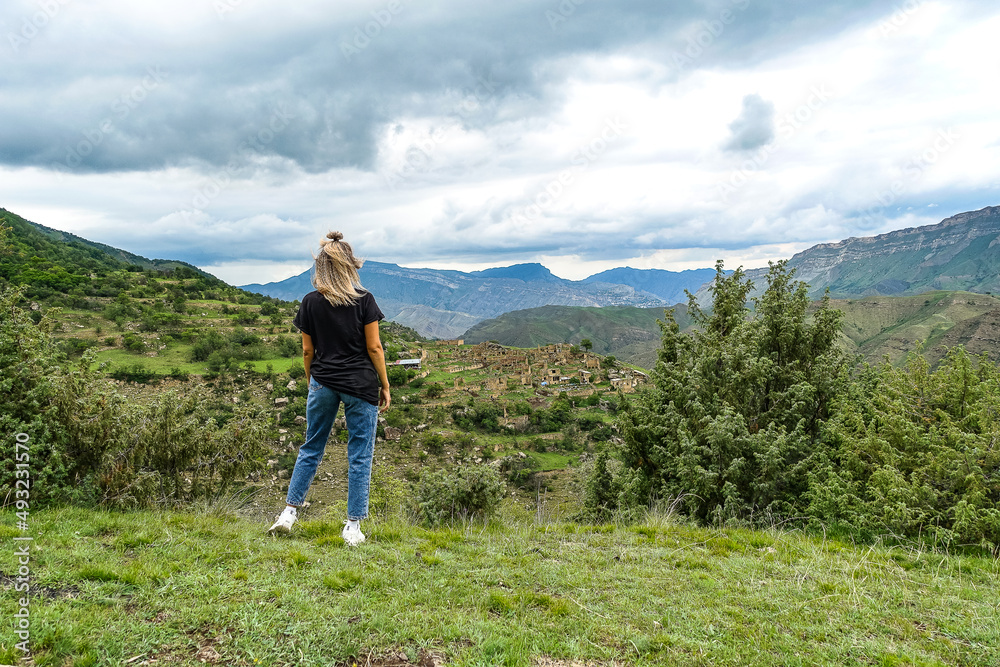 A girl on the background of the village of Kurib in the Caucasus mountains, on top of a cliff. Dagestan Russia June 2021