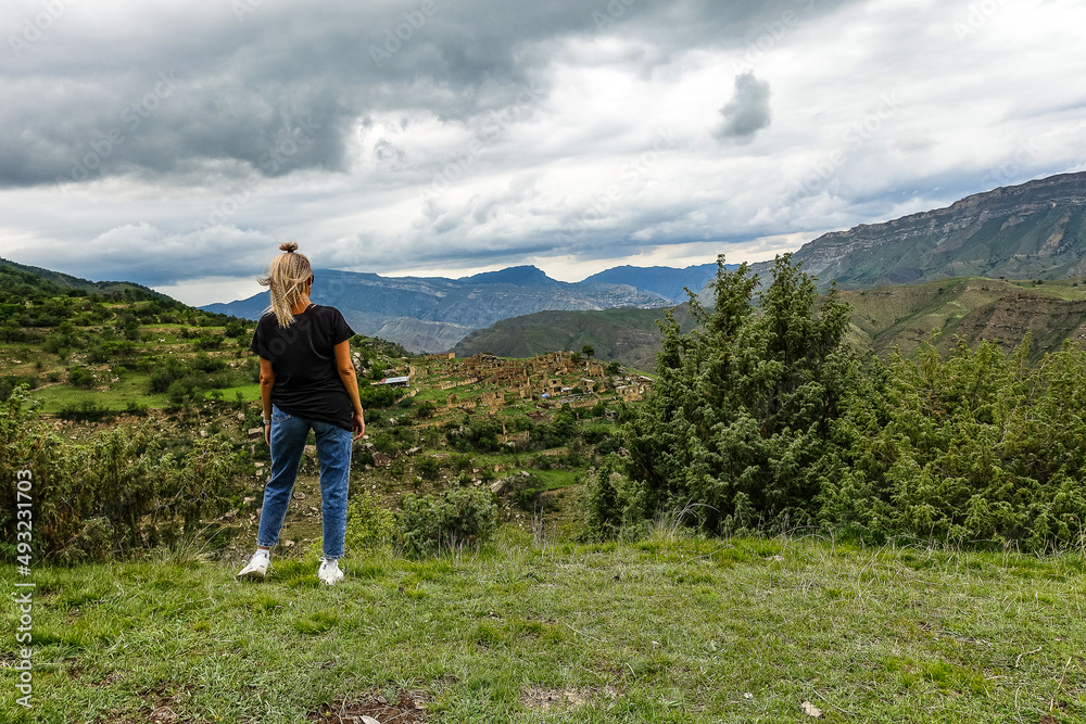 Naklejka premium A girl on the background of the village of Kurib in the Caucasus mountains, on top of a cliff. Dagestan Russia June 2021