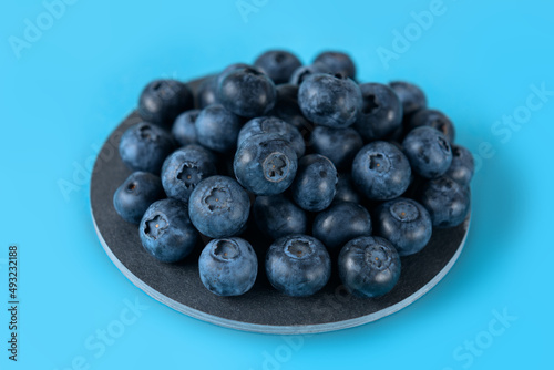 Fresh blueberries on a gray round ceramic board on a blue background. Horizontal.