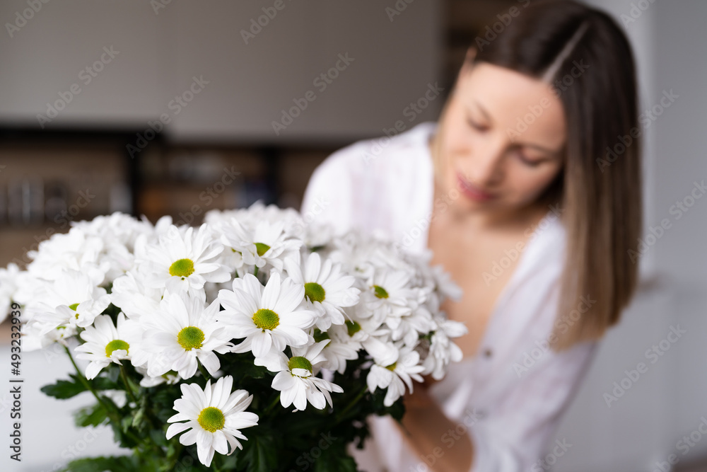 Happy and joyful young woman in white arranging white flowers at home in the kitchen Happy and joyful young woman in white arranging white flowers at home in the kitchen