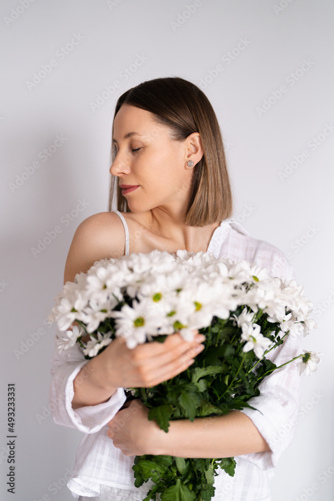 Young beautiful cute sweet lovely smiling woman with hold a bouquet of white fresh flowers on white wall background