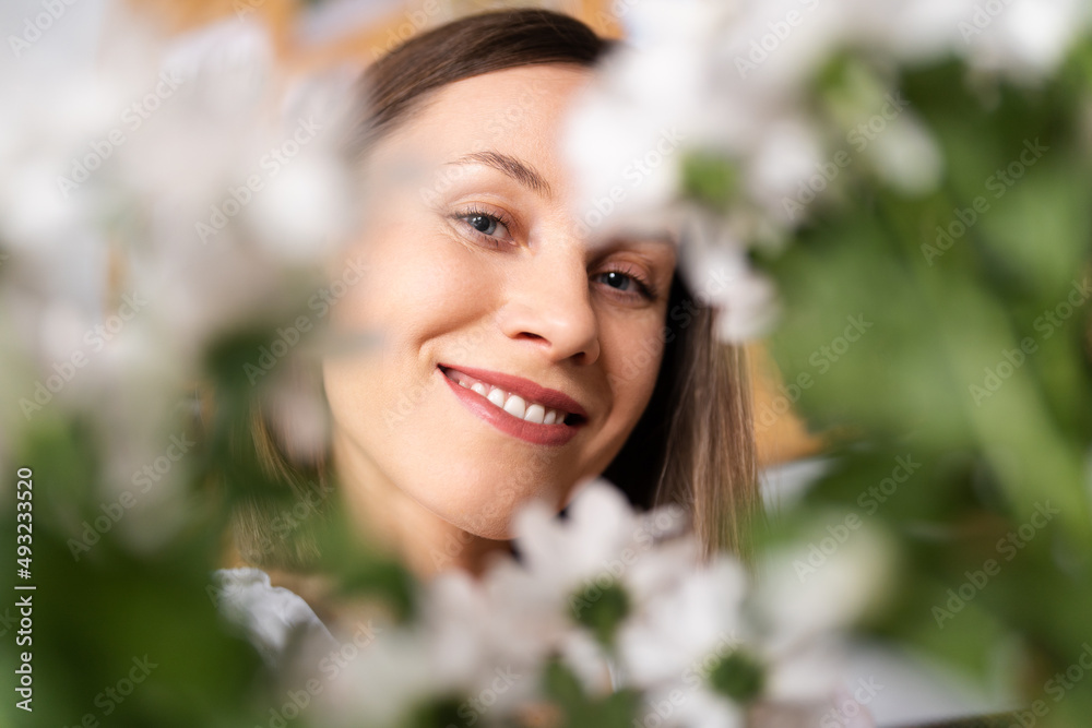 Smiling face of a beautiful young woman surrounded by white flowers and green leaves Smiling face of a beautiful young woman surrounded by white flowers and green leaves