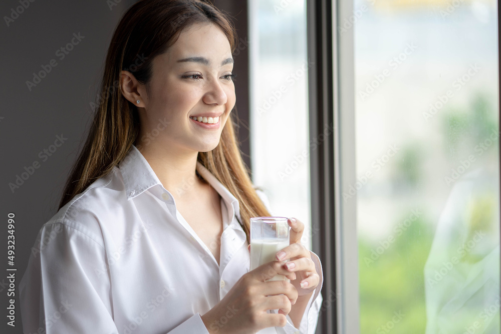 Young beautiful woman looking out window enjoying fresh new day feeling rested and drinking glass of milk. Young beautiful woman looking out window enjoying fresh new day feeling rested and drinking glass of milk.