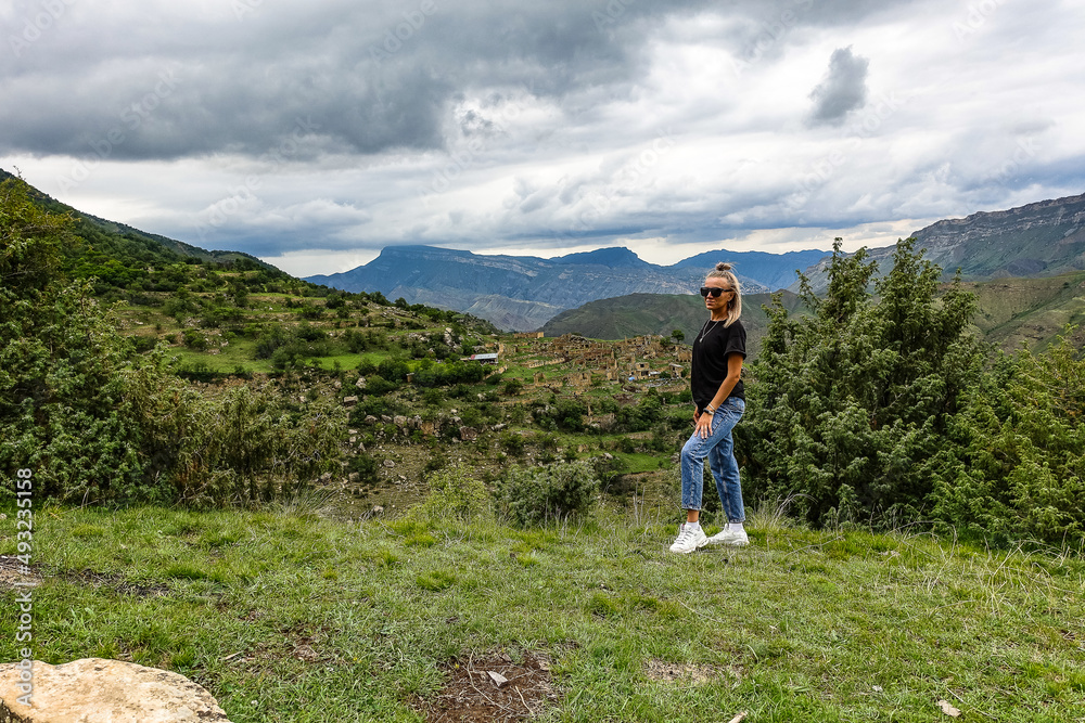 Naklejka premium A girl on the background of the village of Kurib in the Caucasus mountains, on top of a cliff. Dagestan Russia June 2021