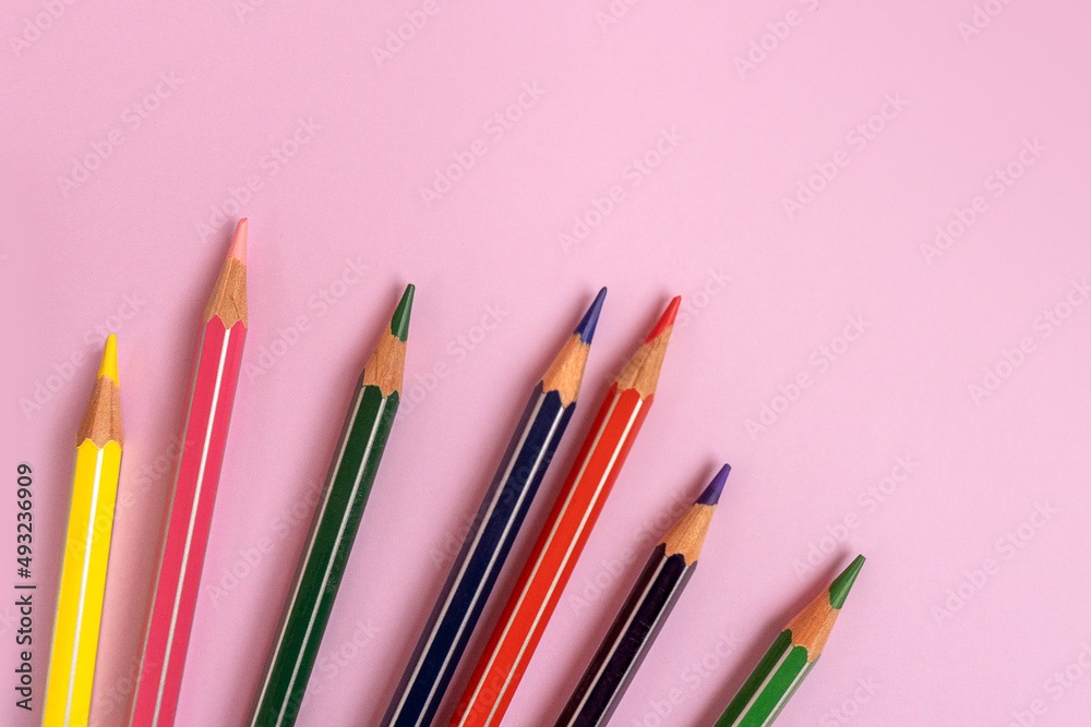 Color pencils on a light pink background. Top view with space for text. Back to school concept. Flat lay stationery mockup. Bright backplate for your design. Spectrum of different colors