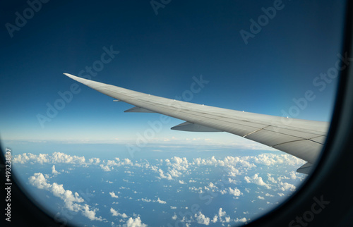 Wing of an airplane flying over morning clouds. View on cloud and blue sky through the airplane window.