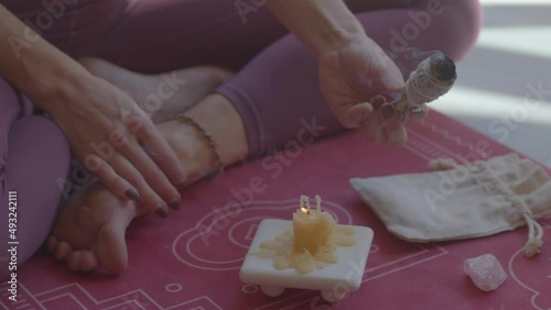 Still anonymous close-up footage of a blond caucasian young female preparing ambient for a yoga practice at home on a sunny day. Burning sage sticks in a lotus pose. 4k high-quality video