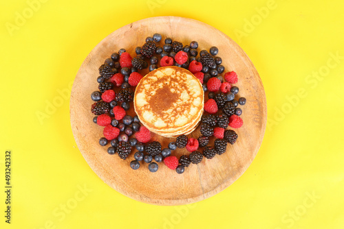 Pancakes with red fruits: blueberries, raspberries and blackberries on a colorful  background 