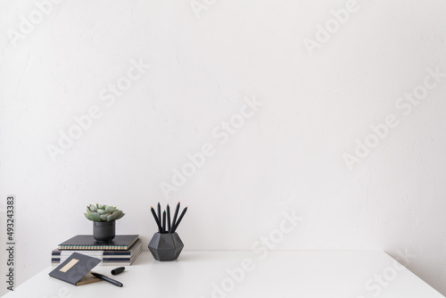 Front view white desk with supplies  mug and white wall copy space..