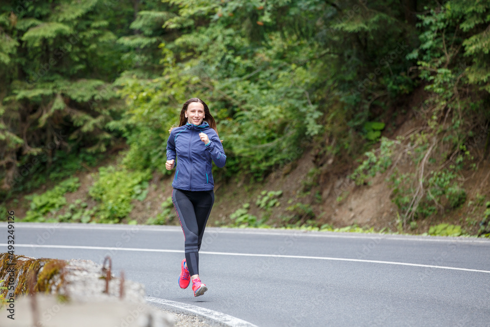 Runner woman running on the mountain road through the forest. Runner woman running on the mountain road through the forest.