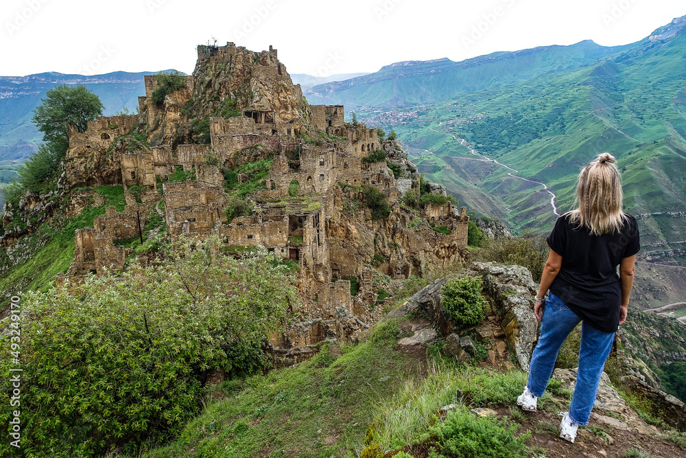A girl on the background of Gamsutl village in the Caucasus mountains, on top of a cliff. Dagestan Russia June 2021