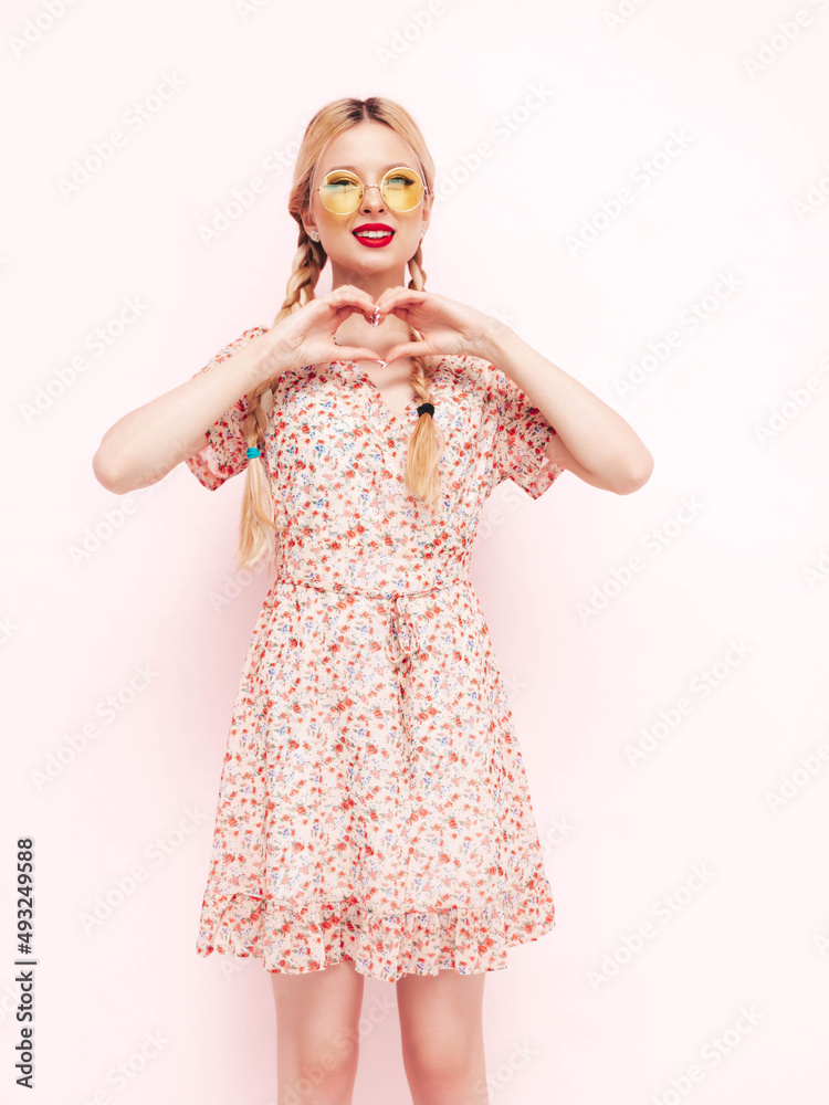 Young beautiful smiling female in trendy summer red dress. Sexy carefree blond woman posing near wall in studio. Positive model having fun. Cheerful and happy in sunglasses. Makes heart sign Young beautiful smiling female in trendy summer red dress. Sexy carefree blond woman posing near wall in studio. Positive model having fun. Cheerful and happy in sunglasses. Makes heart sign