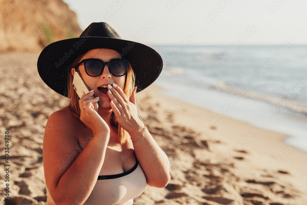 Young Woman Emotionally Expresses Surprise While Talking on the Phone on Sandy Beach by the Sea