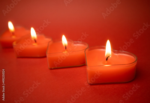 Burning heart-shaped candles with blazing flames, red background Valentine's Day