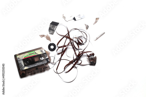 This shows a well known problem with the old fashioned compact cassettes: the tape used to come out, making the cassette useless. Vintage compact cassette tape on white background.