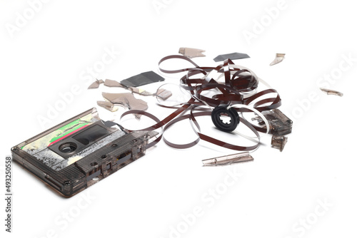 This shows a well known problem with the old fashioned compact cassettes: the tape used to come out, making the cassette useless. Vintage compact cassette tape on white background.