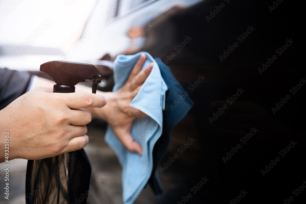 Car clean concept, Hand a man holding clean spray wax and microfiber clenning car body cloth to take care of the surface of the car from washing