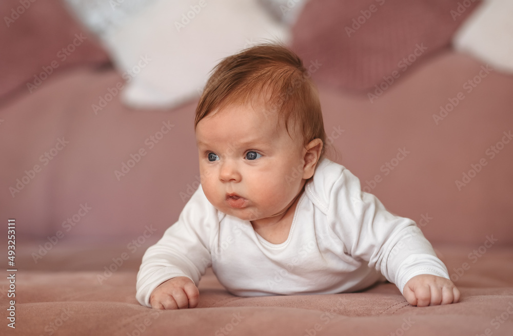 Baby girl wearing white clothes in sunny nursery room. Newborn child relaxing on sofa. Baby girl wearing white clothes in sunny nursery room. Newborn child relaxing on sofa.
