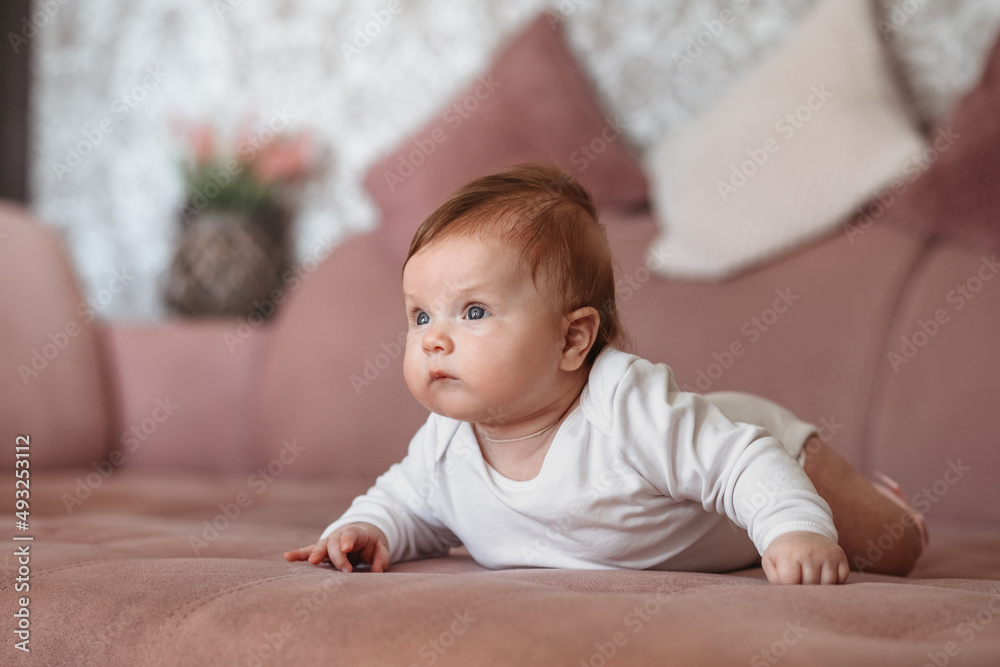 Baby girl wearing white clothes in sunny nursery room. Newborn child relaxing on sofa. Baby girl wearing white clothes in sunny nursery room. Newborn child relaxing on sofa.