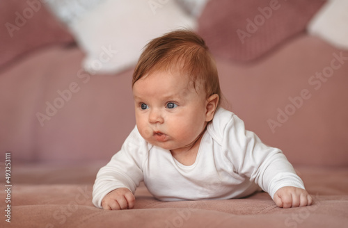 Baby girl wearing white clothes in sunny nursery room. Newborn child relaxing on sofa.