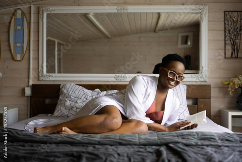 A beautiful young african-american woman is reading a book in her lingerie on the bed.