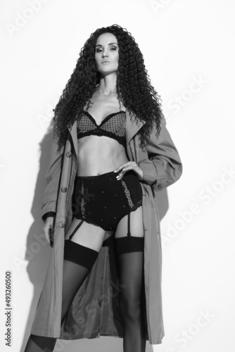 Sexy girl posing in lingerie and coat against a white wall. Black and white photo