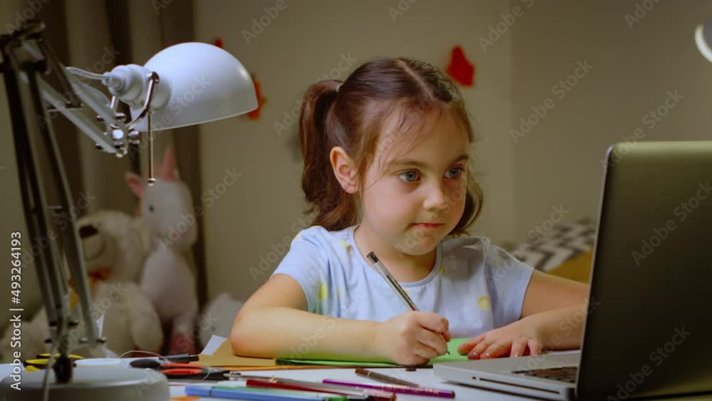 Preschool girl is studying at an online school at home with a laptop.
