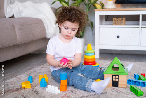curly child girl playing with pyramid and constructor at home. early children development