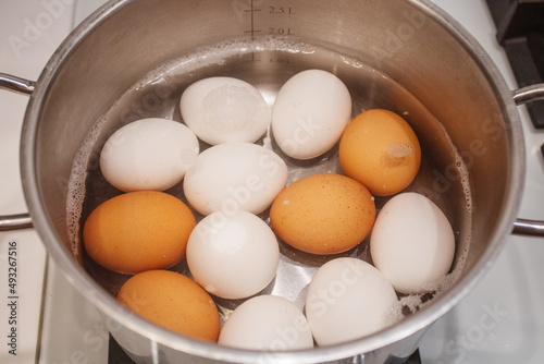 The process of boiling white eggs in a stainless saucepan of bubbling water on black background. The preparation for painting of eggs before Easter Holiday.