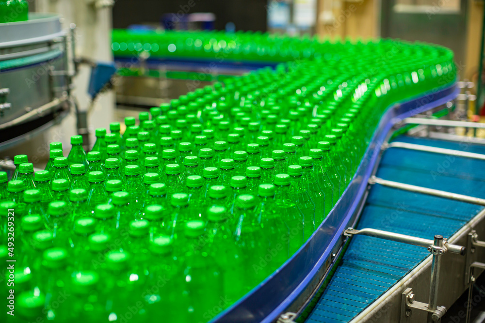 Fototapeta premium Beverage factory interior. Conveyor flowing with bottles for juice green